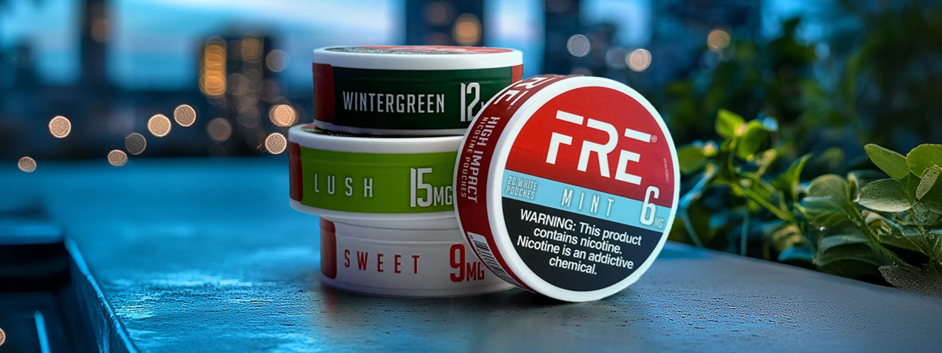FRE nicotine pouches in Mint, Lush, Sweet and Wintergreen stacked on a table with a cityscape background