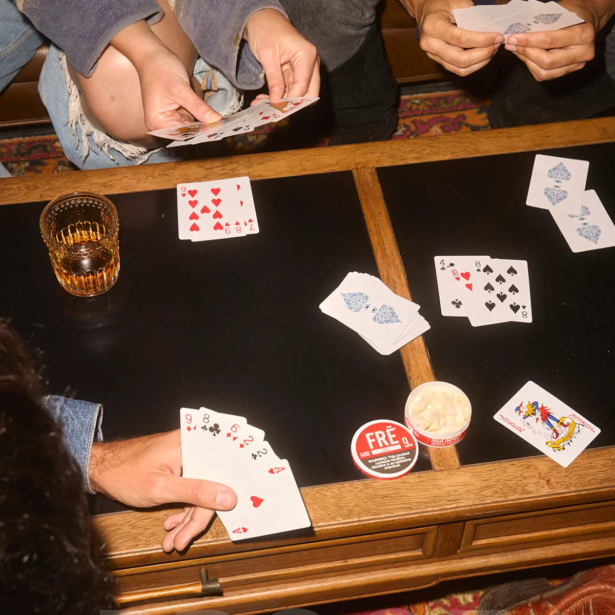FRE Pouch nicotine tin on a table during a card game with friends, highlighting the brand’s discreet, social, and tobacco-free nicotine experience