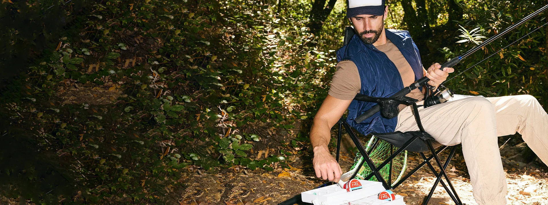 Man in trucker hat and vest fishing, reaching for FRE nicotine pouches in his tackle box