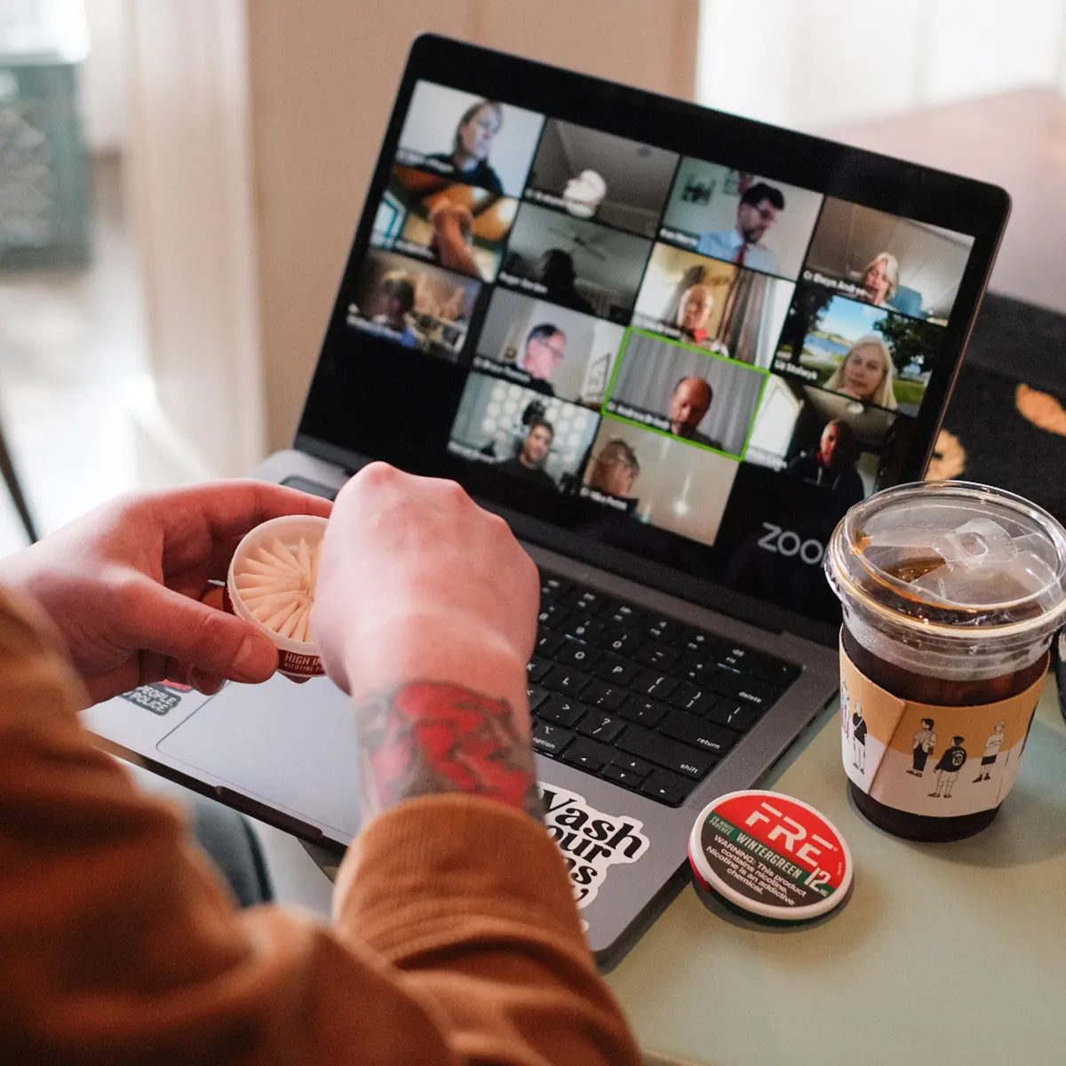 Person opening a FRE Pouch nicotine tin while on a Zoom video call with coffee, highlighting a discreet, tobacco-free option for work-from-home productivity